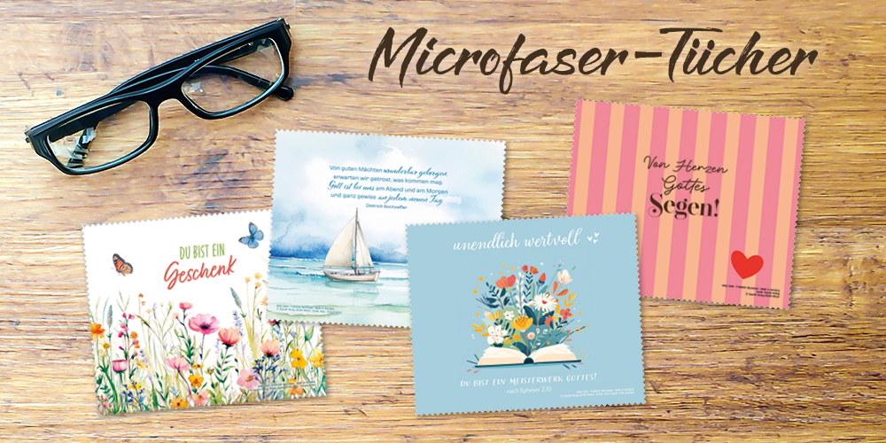 Eine Brille auf einem Holztisch, daneben vier bunt gestaltete Mikrofaser-Tücher mit verschiedenen Motiven, mit Sprüchen, Versen und Zitaten. Text: Microfaser-Tücher