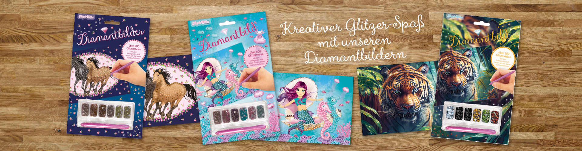 Dunkler Holzhintergrund, darauf: Drei Diamantbilder mit Pferde-, Meerjungfrauen- und Tigermotiv und Paletten mit Glitzersteinen.
