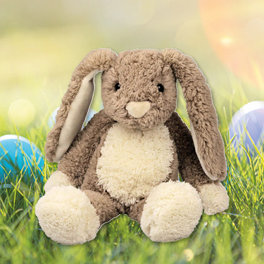 Kuscheltier Hase 'Schnuffel' sitzend auf einer Wiese mit Ostereiern