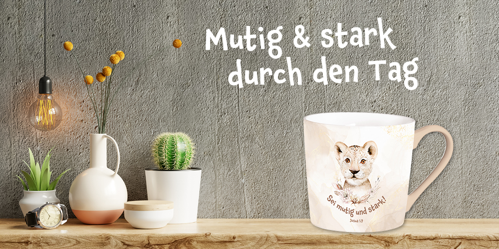 Rosa-beige-farbene Tasse mit Aquarell-Löwin-Motiv, auf einem Tisch vor einer grauen Wand, links sind Töpfe, eine Lampe und Armbanduhr. Text: „Mutig & stark durch den Tag.“