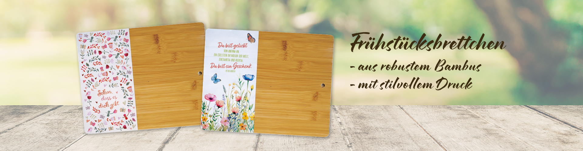 Banner mit einem Holztisch, vor einem grünen Park mit Baum, auf dem Tisch stehen zwei schön dekorierte Bambus-Brettchen. Text: „Frühstücksbrettchen, aus robustem Bambus, mit stilvollem Druck“.