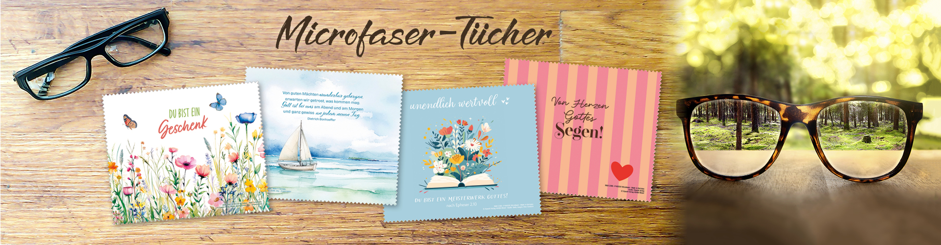 Eine Brille auf einem Holztisch, daneben vier bunt gestaltete Mikrofaser-Tücher mit verschiedenen Motiven, mit Sprüchen, Versen und Zitaten. Text: Microfaser-Tücher