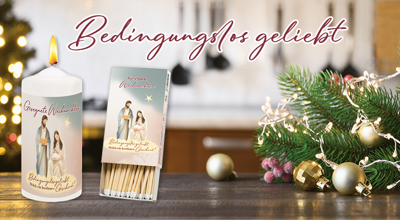 Eine Weihnachtskerze mit Krippenmotiv und der passenden Streichholz-Schachtel stehen auf einem weihnachtlich geschmückten Tisch mit Tannenzweigen, im verschwommenen Hintergrund ist eine Küche und ein Weihnachtsbaum erkennbar.