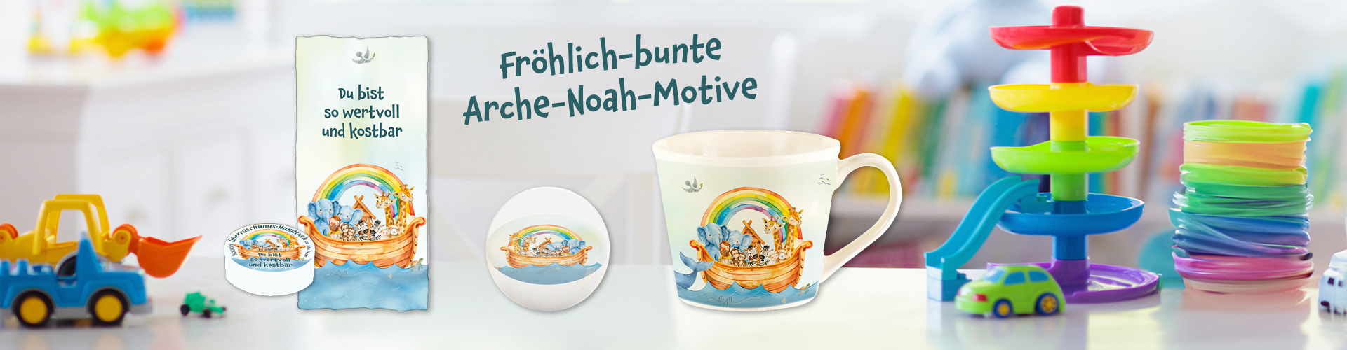 Bunter Banner mit Arche-Noah-Motiven auf Tasse, einem Überraschungs-Handtuch und einem Flummi, umgeben von Spielzeug, in einem Kinderzimmer.