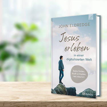 Das Buch ‚Jesus erleben in einer digitalisierten Welt‘ von John Eldredge auf einem Holztisch.