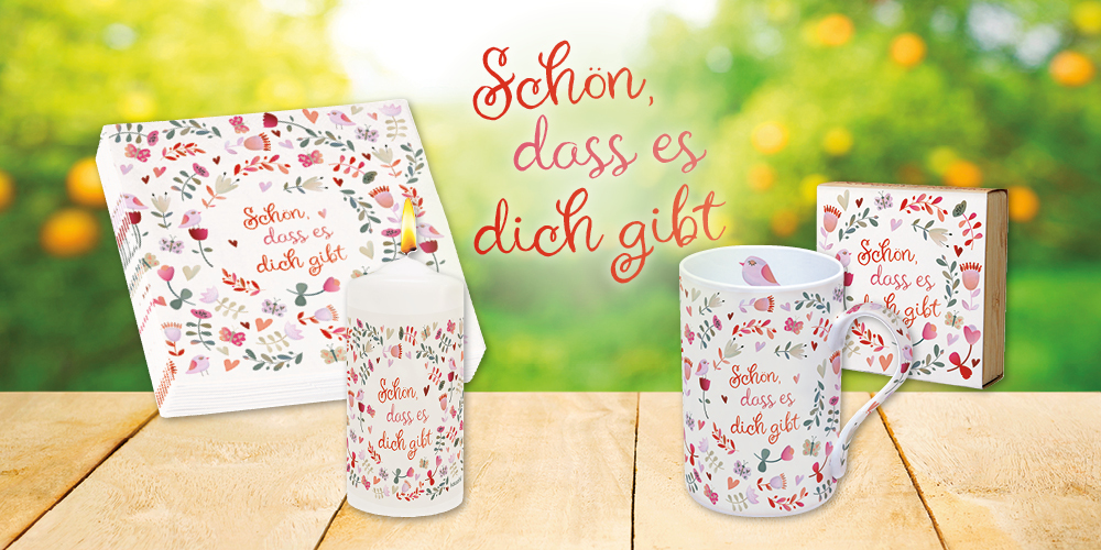 Banner mit Tisch vor frühlingshaftem Hintergrund, mit einer Tasse, Servietten, Kerze, Bambus-Teelichthalter und Karte mit dem gleichen grafischen, frühlingshaften Motiv. Text: Schön, dass es dich gibt.