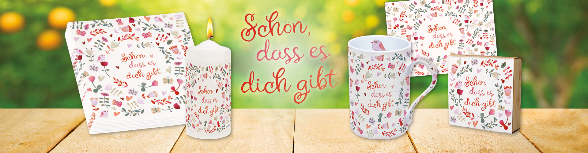 Banner mit Tisch vor frühlingshaftem Hintergrund, mit einer Tasse, Servietten, Kerze, Bambus-Teelichthalter und Karte mit dem gleichen grafischen, frühlingshaften Motiv. Text: Schön, dass es dich gibt.