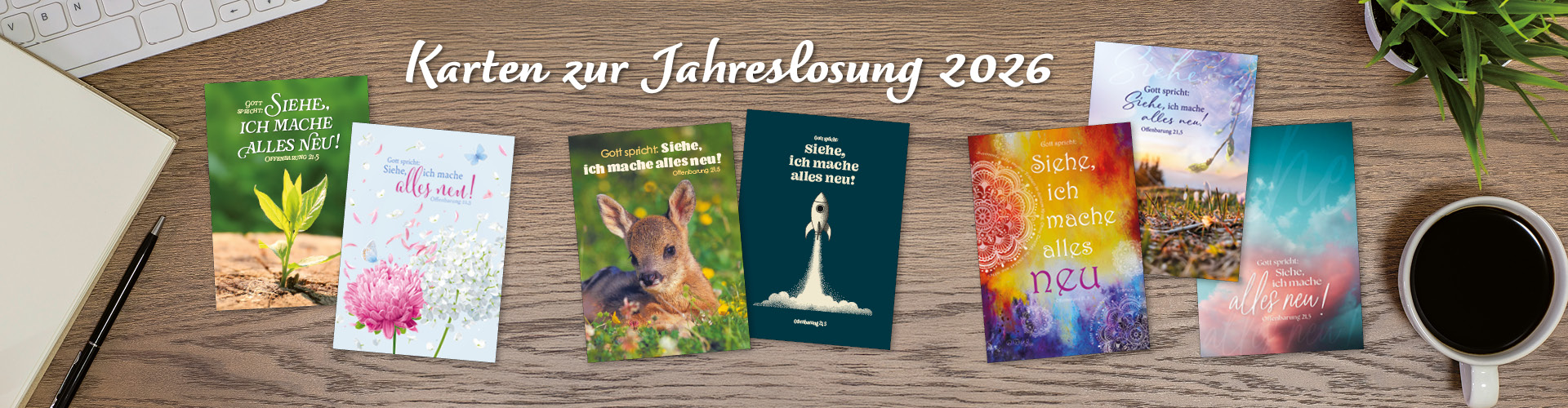 Banner mit Karten zur Jahreslosung 2026, die verschiedene Motive zeigen, auf einem Holztisch mit Schreibutensilien.