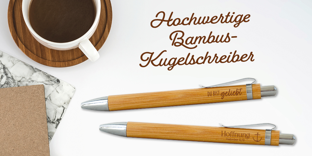 Ein Schreibtisch-Setup mit einer Tastatur, einer Tasse Kaffee auf einem Holzuntersetzer, einem Notizbuch und zwei Bambus-Kugelschreibern. Text: Hochwertige Bambus-Kugelschreiber