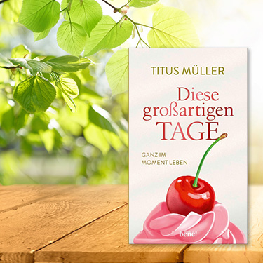 Buchtitel 'Diese großartigen Tage' von Titus Müller auf einem Tisch unter einem Baum, Äste und Blätter im Hintergrund.